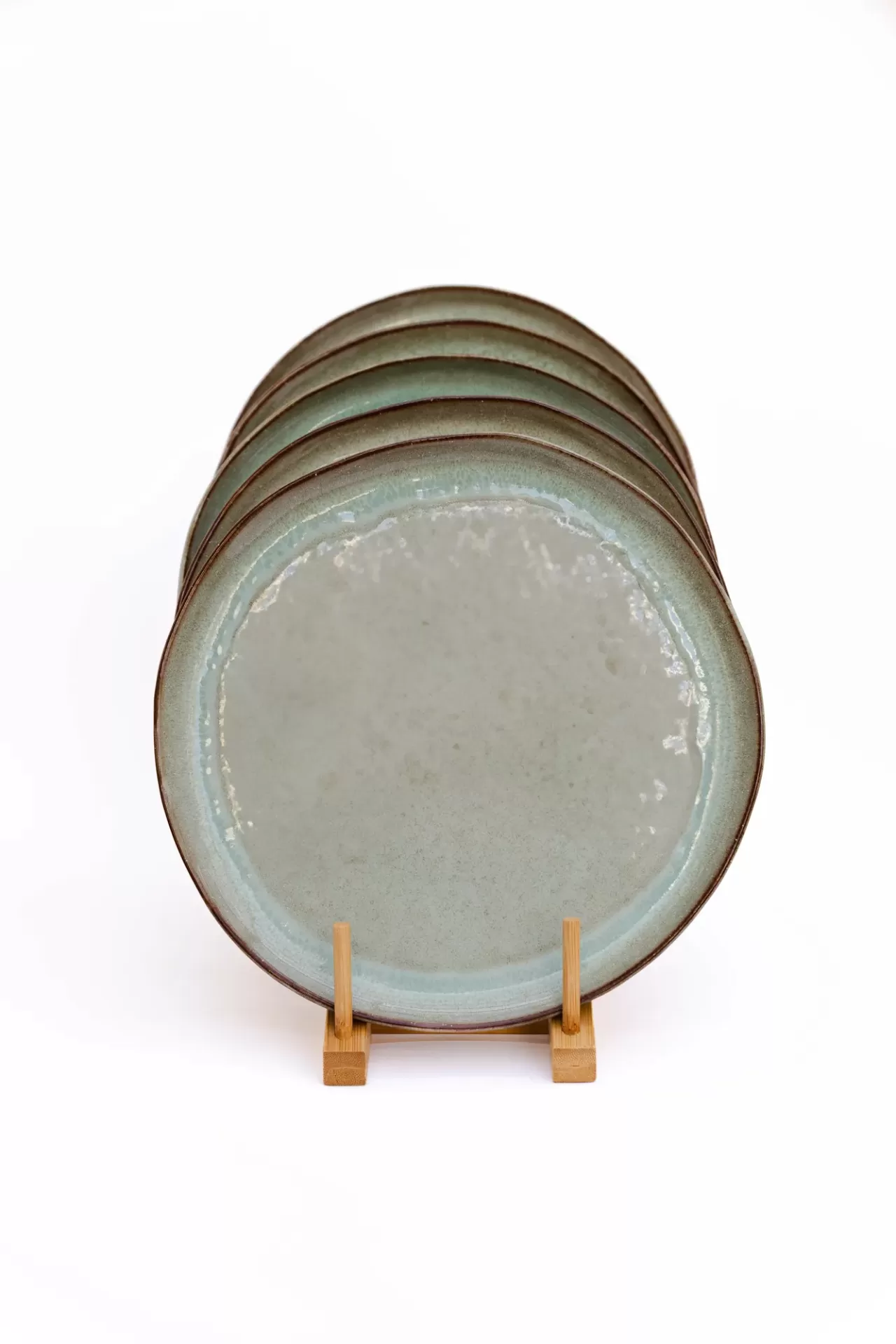 Cinco pratos de cerâmica verde claro com bordas irregulares em suporte de madeira