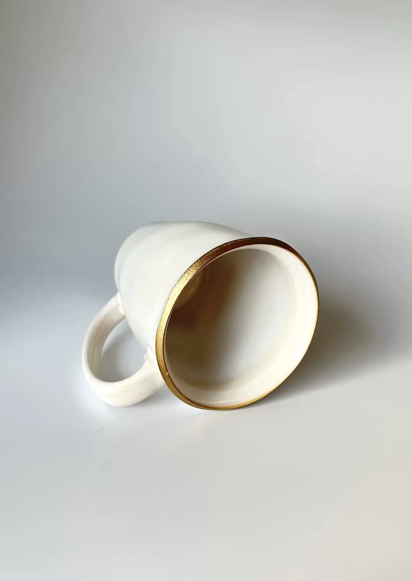 Caneca branca com borda dourada deitada num fundo branco
