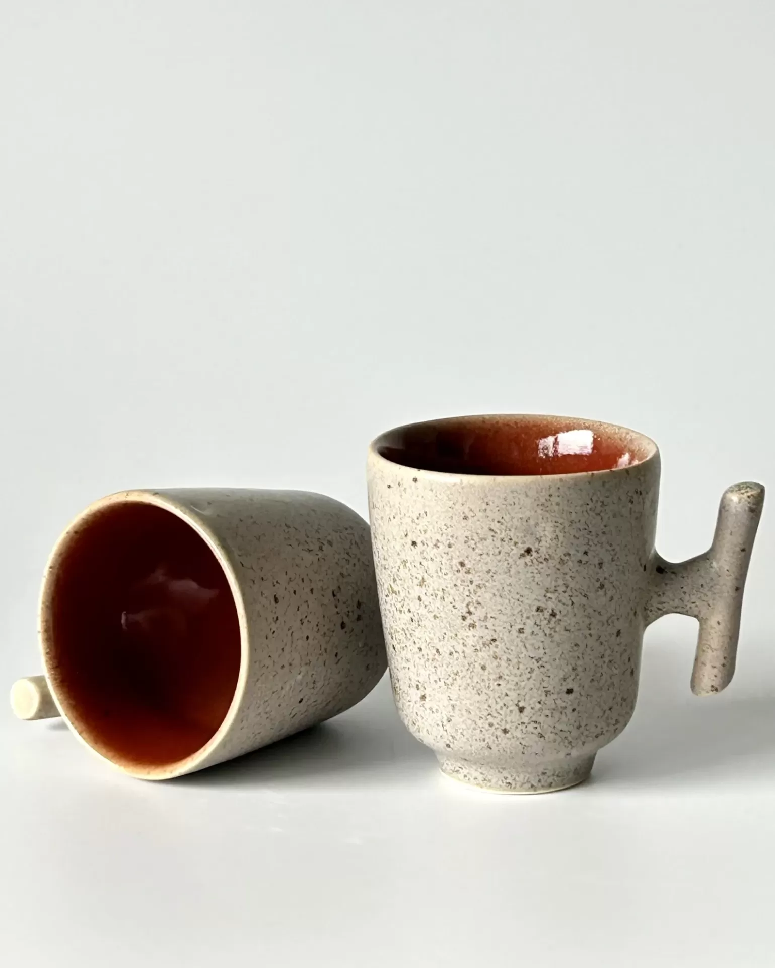 Duas chávenas de cerâmica cinzentas com interior laranja, uma de pé e outra deitada