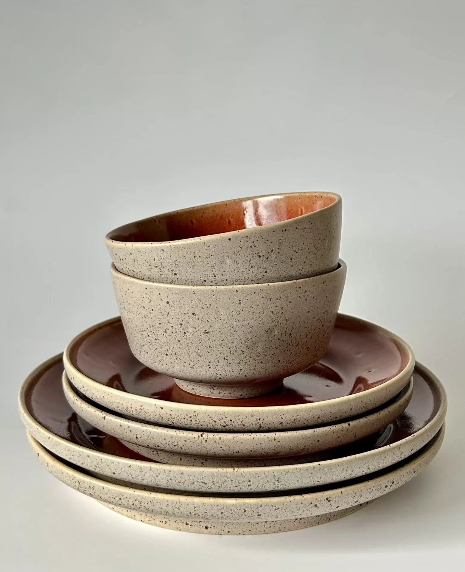 Conjunto de loiça cerâmica com tigelas e pratos em tons bege e castanho avermelhado.