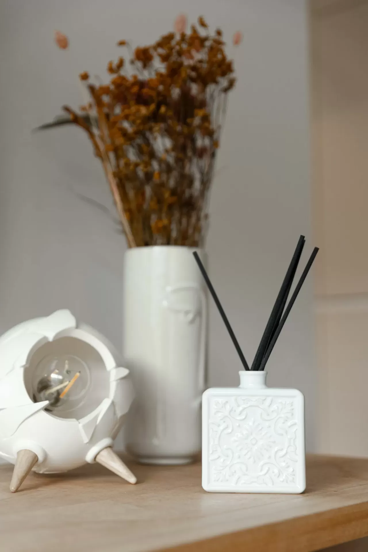 Relógio branco moderno, frasco branco decorativo com paus pretos, vaso branco com flores secas castanhas