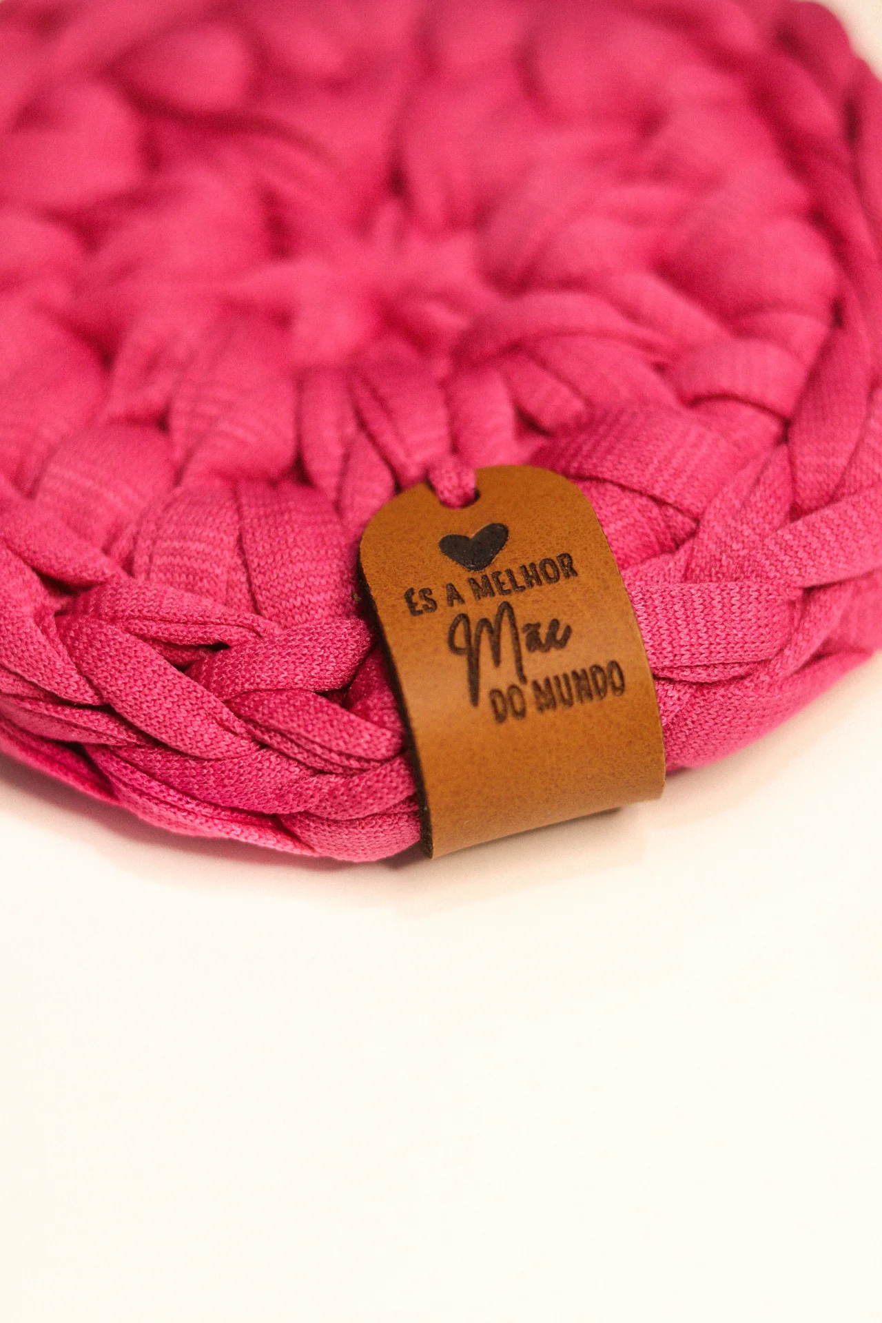 Produto têxtil rosa com etiqueta de couro castanho com texto em português.