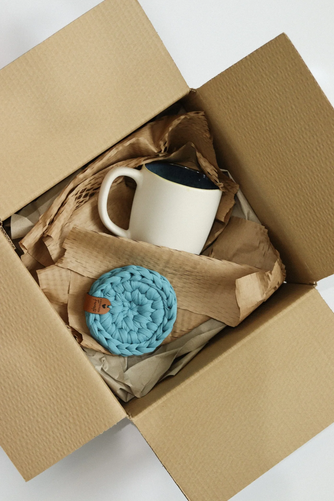 Caixa de cartão aberta com caneca branca e porta-copos azul