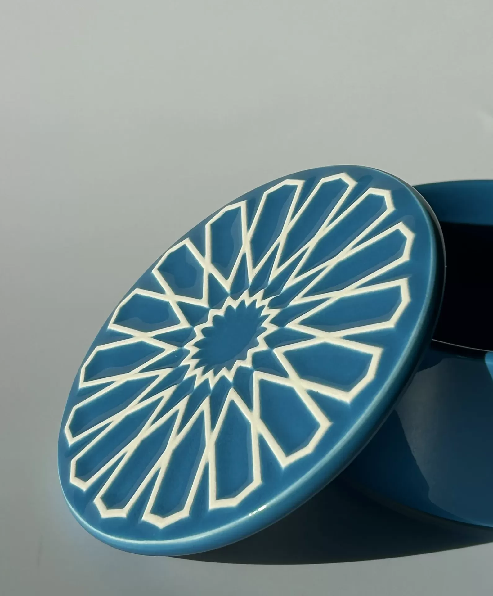 Caixa azul de cerâmica com tampa decorativa geométrica branca.