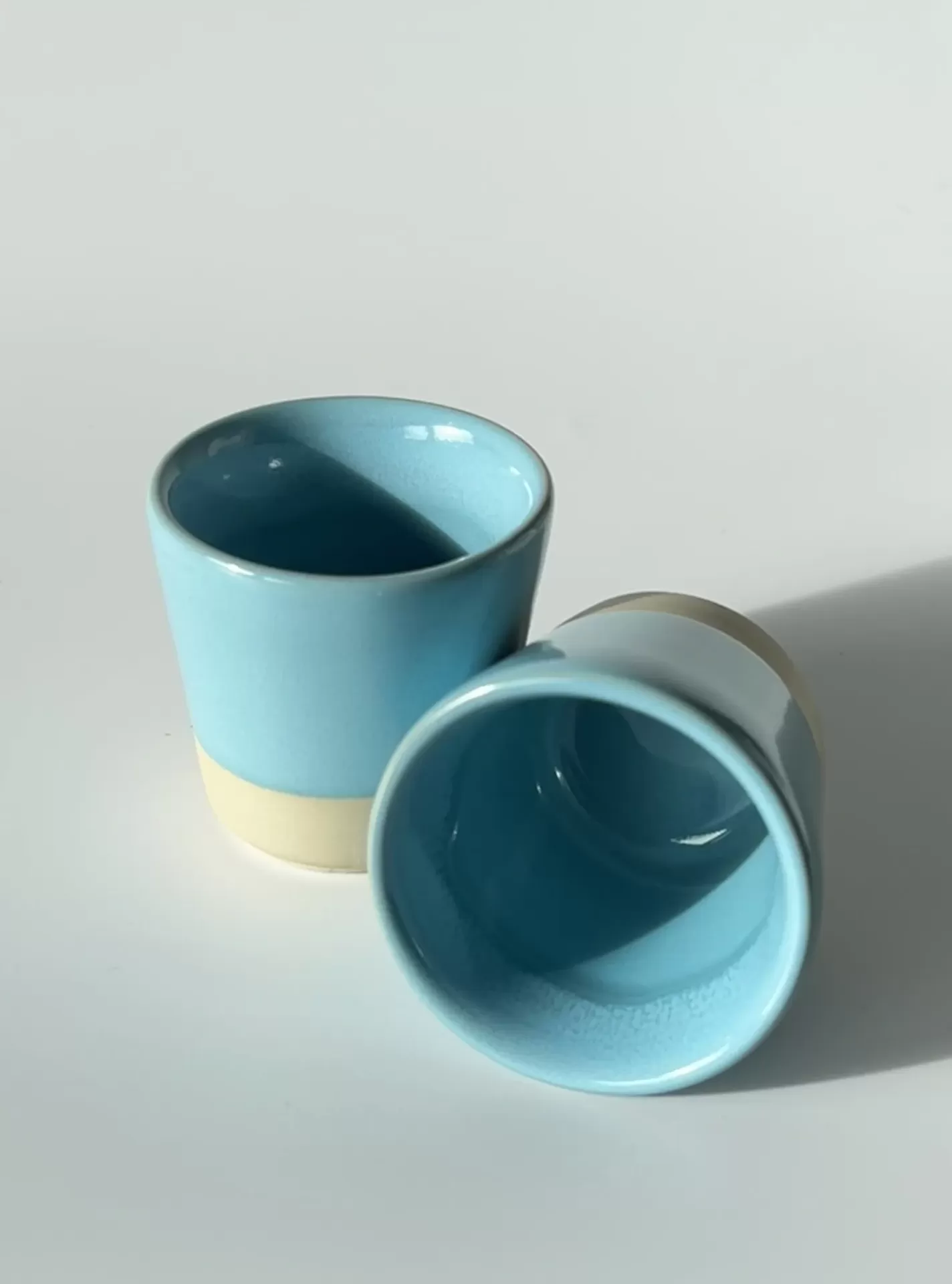 Dois copos pequenos azuis celeste com base bege sobre mesa branca