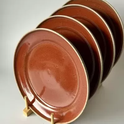 Conjunto de quatro pratos redondos castanho-avermelhados em suporte de madeira