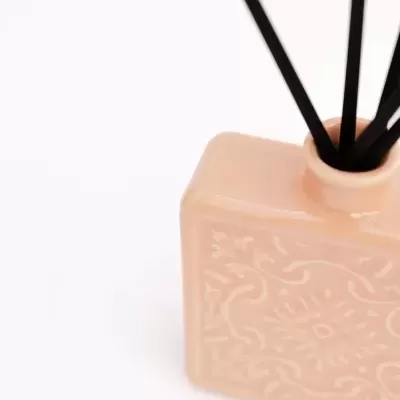 Recipiente de cerâmica bege com padrão floral e pauzinhos de difusor pretos