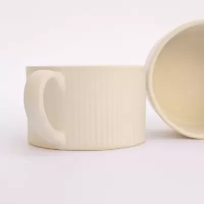 Duas canecas cerâmicas brancas com textura de linhas verticais, uma em pé e outra deitada de lado