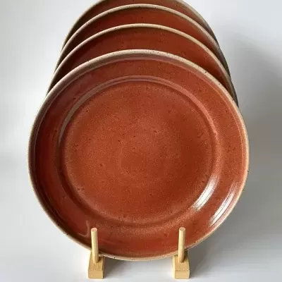 Conjunto de quatro pratos de cerâmica terracota em suporte de madeira.