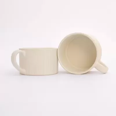Dois copos de cerâmica bege com textura riscada verticalmente, um virado mostrando interior e outro em posição normal