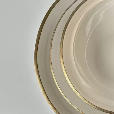 Três pratos cerâmicos creme com bordas douradas sobre superfície branca