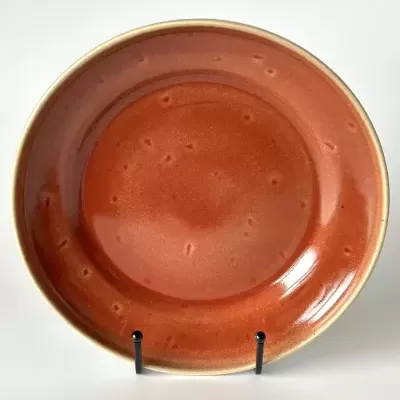 Prato cerâmico laranja com textura pontilhada em suporte preto