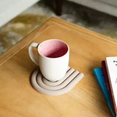 Copo branco com interior rosa sobre suporte de silicone bege em mesa de madeira