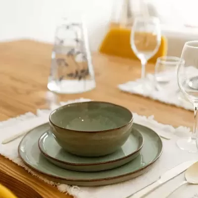 Conjunto de louça verde fosca numa mesa de madeira com copos e talheres