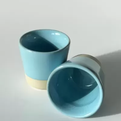 Dois copos pequenos azuis celeste com base bege sobre mesa branca
