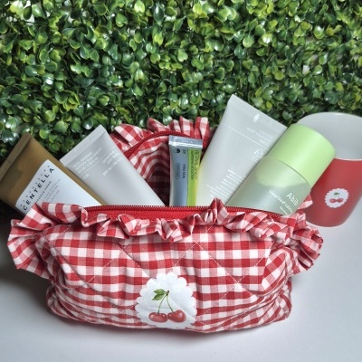 Bolsa de tecido xadrez vermelho e branco com produtos cosméticos em fundo branco e parede verde