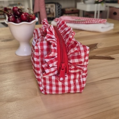 Estojo xadrez vermelho e branco com fecho de correr vermelho sobre mesa de madeira clara