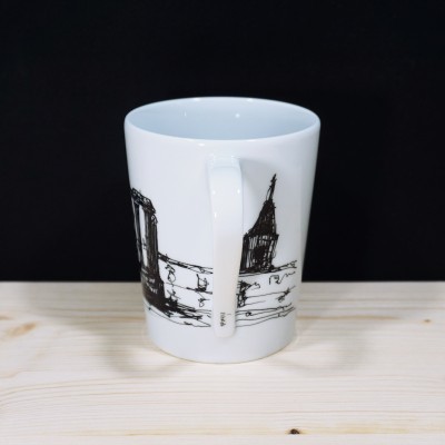 Caneca branca com desenho preto em fundo preto e superfície de madeira clara