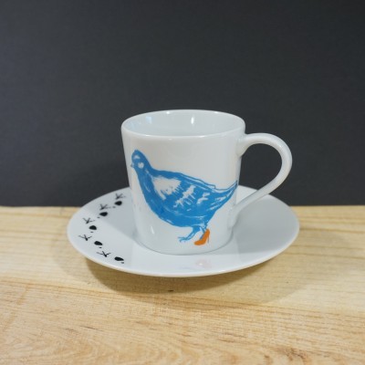 Chávena de café branca com desenho azul de pássaro e pires branco com padrão preto