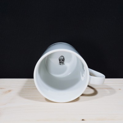 Caneca branca com caveira no interior, numa mesa de madeira clara
