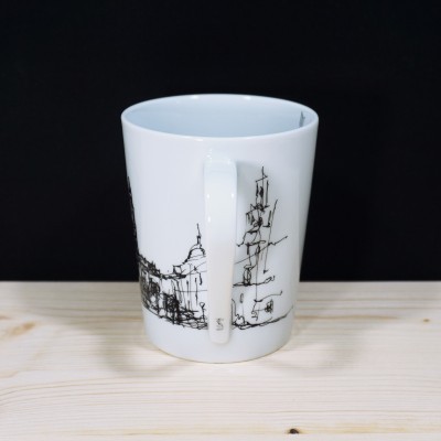 Caneca branca com desenhos pretos de edifícios sobre mesa de madeira