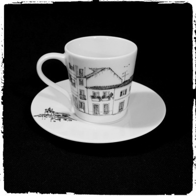 Xícara de café e pires em cerâmica branca com desenho preto de edifícios
