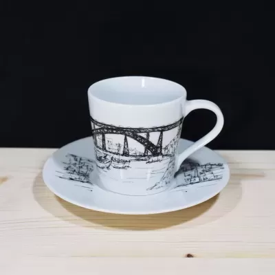 Vista de trás de uma chávena de café de porcelana branca com pires, destacando a cidade do Porto