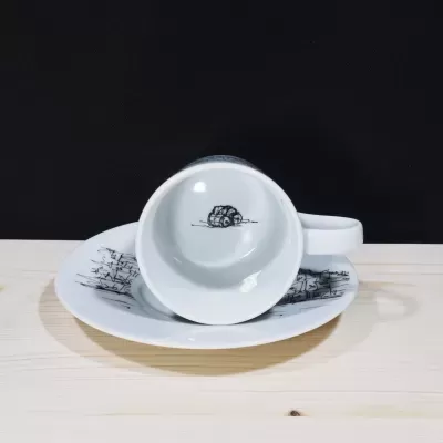 Chávena de café de porcelana branca inclinada sobre o pires, revelando ilustração de três pipas