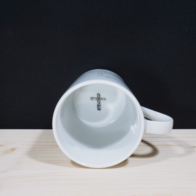 Caneca branca com cruz preta no fundo interior, sobre madeira clara.
