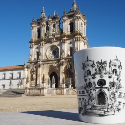Caneca branca com desenho preto de edifício histórico, com edifício monumental ao fundo