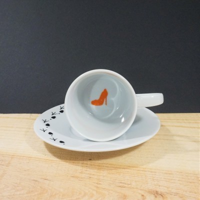 Chávena de porcelana branca com sapato laranja no interior e prato com padrão de cartas