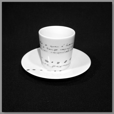 Chávena branca com texto e pegadas pretas sobre pires branco em fundo preto
