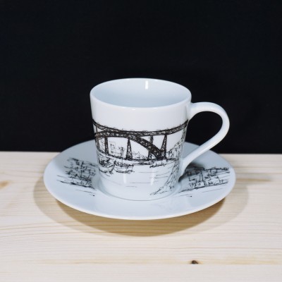 Xícara e pires de cerâmica branca com desenho preto de ponte e barcos
