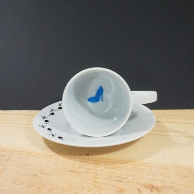 Chávena branca de porcelana com sapato azul no interior e prato com figuras pretas