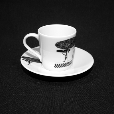 Chávena de café branca com padrão preto sobre pires branco em fundo preto