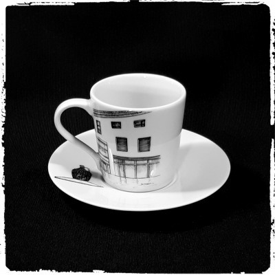 Chávena de café branca com desenho de edifício e pires sobre fundo preto
