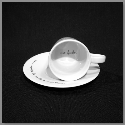 chávena branca com texto preto no interior e pires branco com texto preto sobre fundo preto