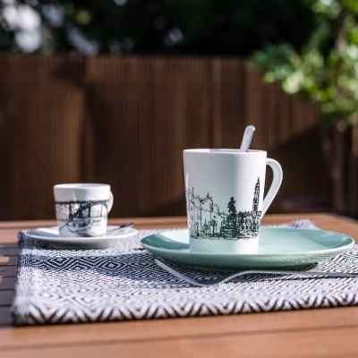 Conjunto de chávenas de café em porcelana com desenhos de paisagens urbanas e pratos sobre uma mesa de madeira