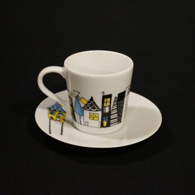 Chávena de café branca com padrão colorido de casas e respectivo pires