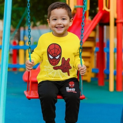 Criança com camisola amarela Homem-Aranha e calças pretas num baloiço vermelho num parque infantil