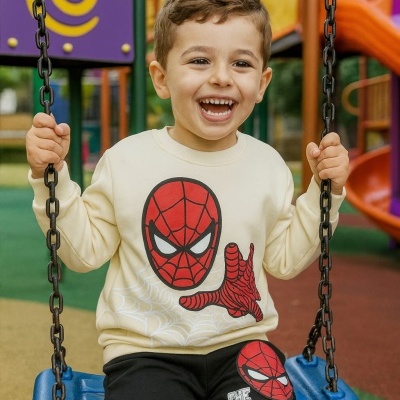 Camisola e calças de criança com estampa do Homem-Aranha sentado num baloiço azul num parque infantil colorido