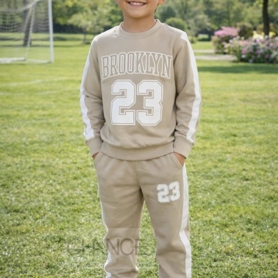 Menino com conjunto desportivo bege com texto BROOKLYN 23, em campo de futebol