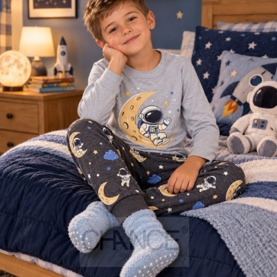 Menino com pijama de astronautas cinza claro sentado em cama com decoração espacial