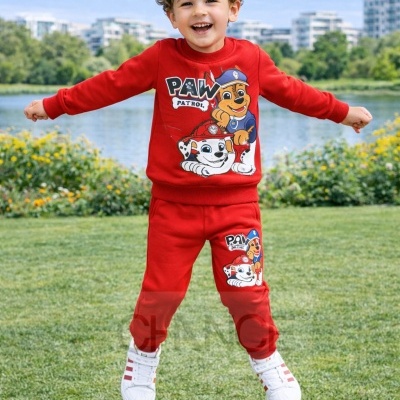 Criança a saltar vestindo conjunto vermelho com personagens da Paw Patrol em ambiente exterior com relvado e lago.
