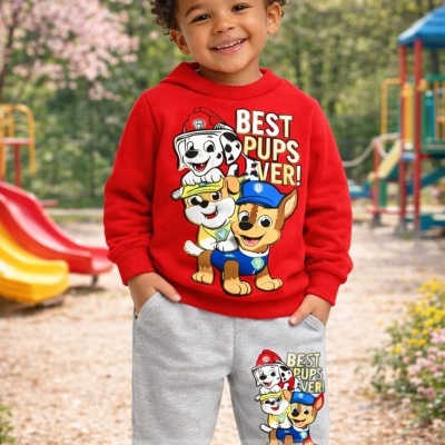 Menino vestido com conjunto infantil vermelho e cinza com desenhos de cães animados, num parque infantil ao ar livre.