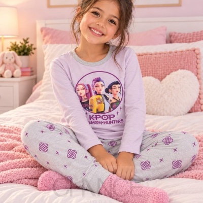 Menina com pijama lilás e cinzento com estampado KPOP sentada numa cama com decoração rosa.