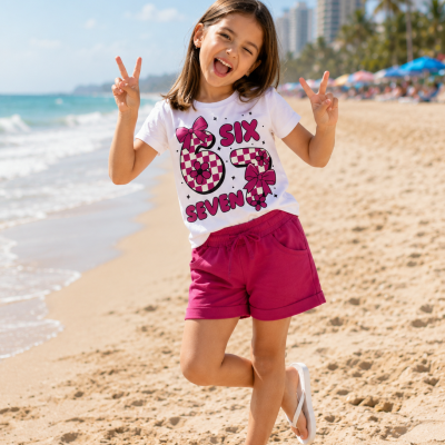 Menina com camiseta branca estampada e short cor-de-rosa na praia com mar e prédios ao fundo