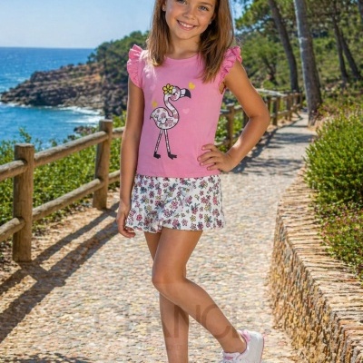 Menina com camisa rosa com flamingo estampado, saia florida branca e sapatilhas brancas com rosa no exterior