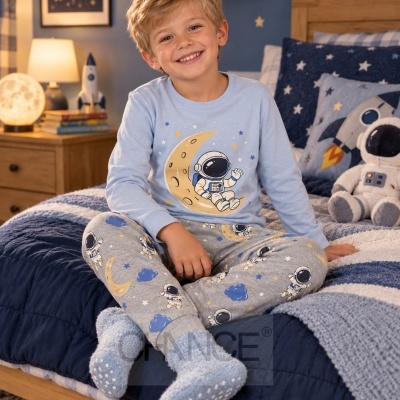 Menino com pijama azul claro e cinza com tema espacial sentado em cama azul