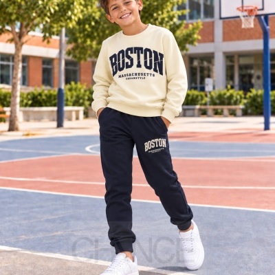 Menino a vestir fato de treino bege e azul escuro com texto Boston num campo de basquetebol